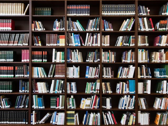 大学图书馆内研究生在台灯下精读学术文献，书桌上摆放着多本学术期刊与笔记本，暖黄灯光营造出专注的学术研究氛围